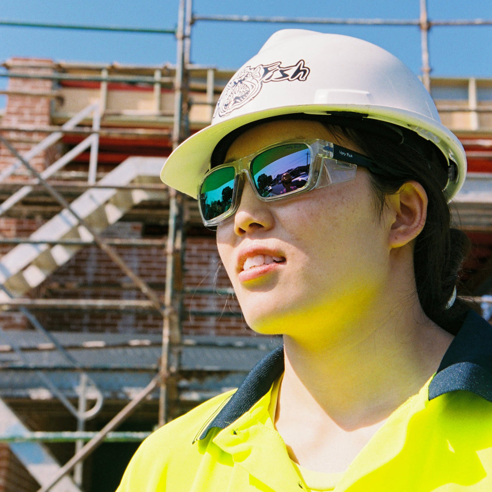 Person wearing a white hard hat and Ugly Fish Safety sunglasses with scaffolding in the background