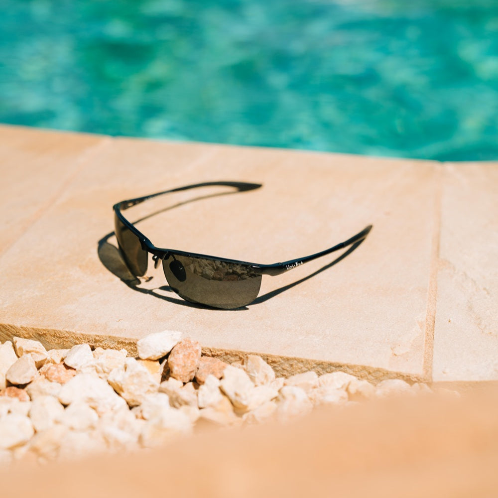 Ugly Fish metal sunglasses on a stone ledge with a pool in the background