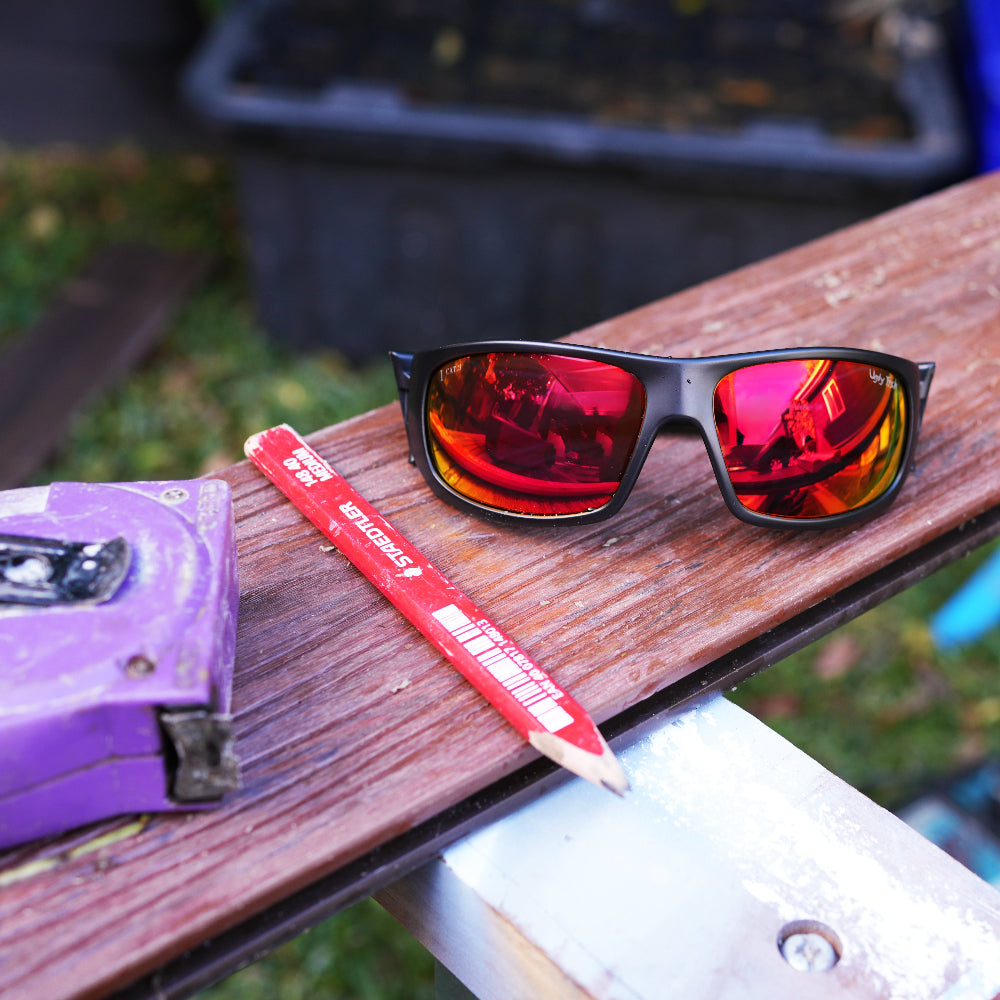 Ugly Fish Safety Sunglasses with red-revo lenses, a purple tape measure, and a red pencil on a wooden surface.