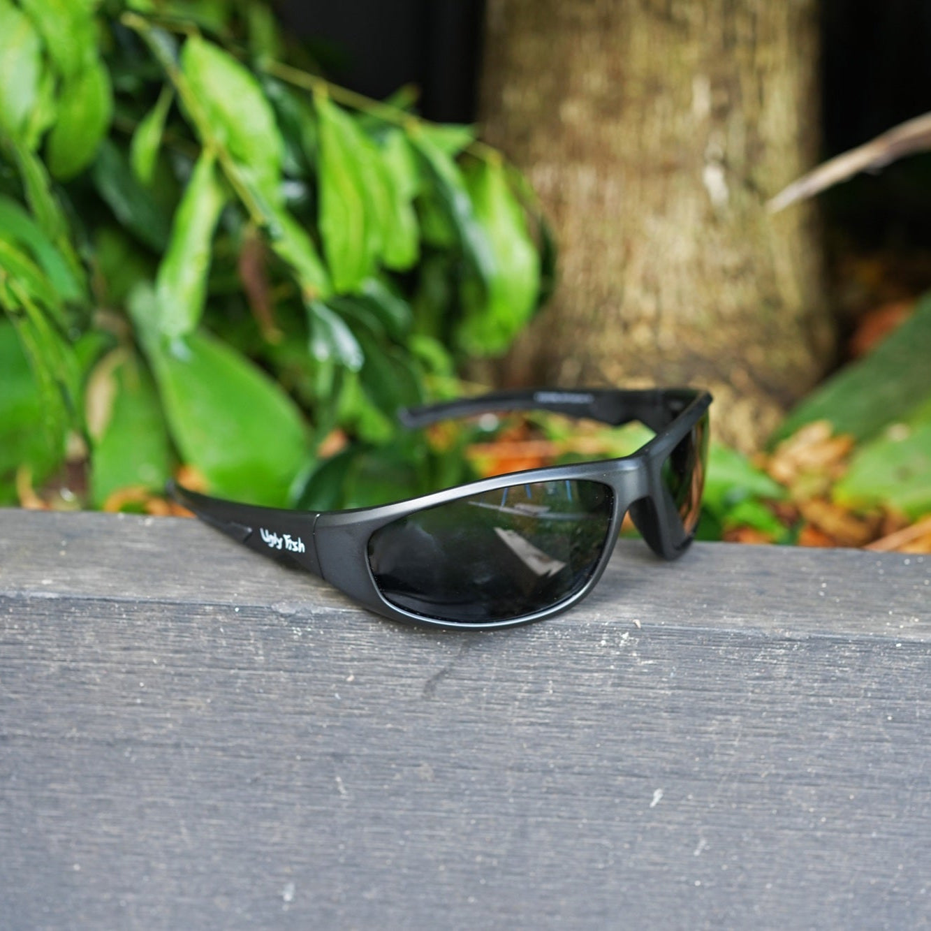 Ugly Fish Safety sunglasses on a wooden surface with green foliage in the background
