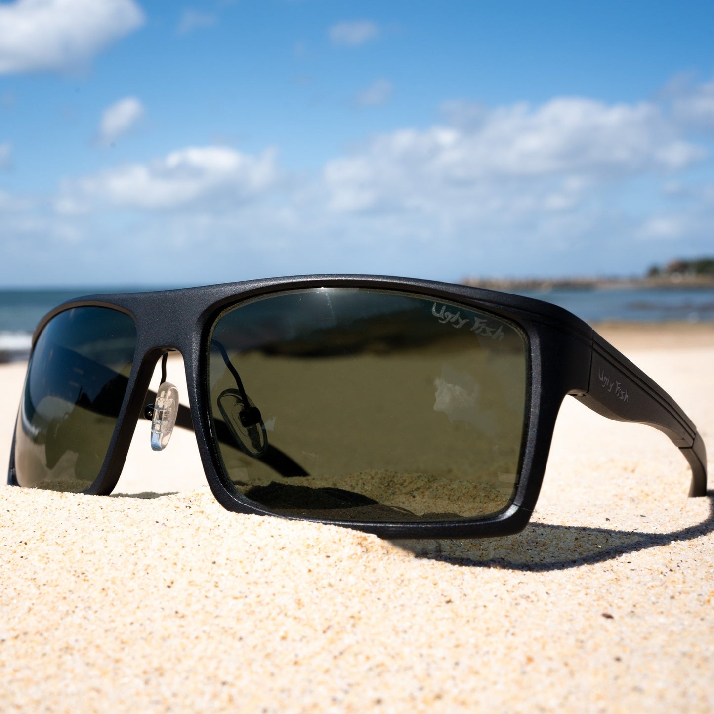 Ugly Fish Sunglasses on a sandy beach with ocean and sky in the background