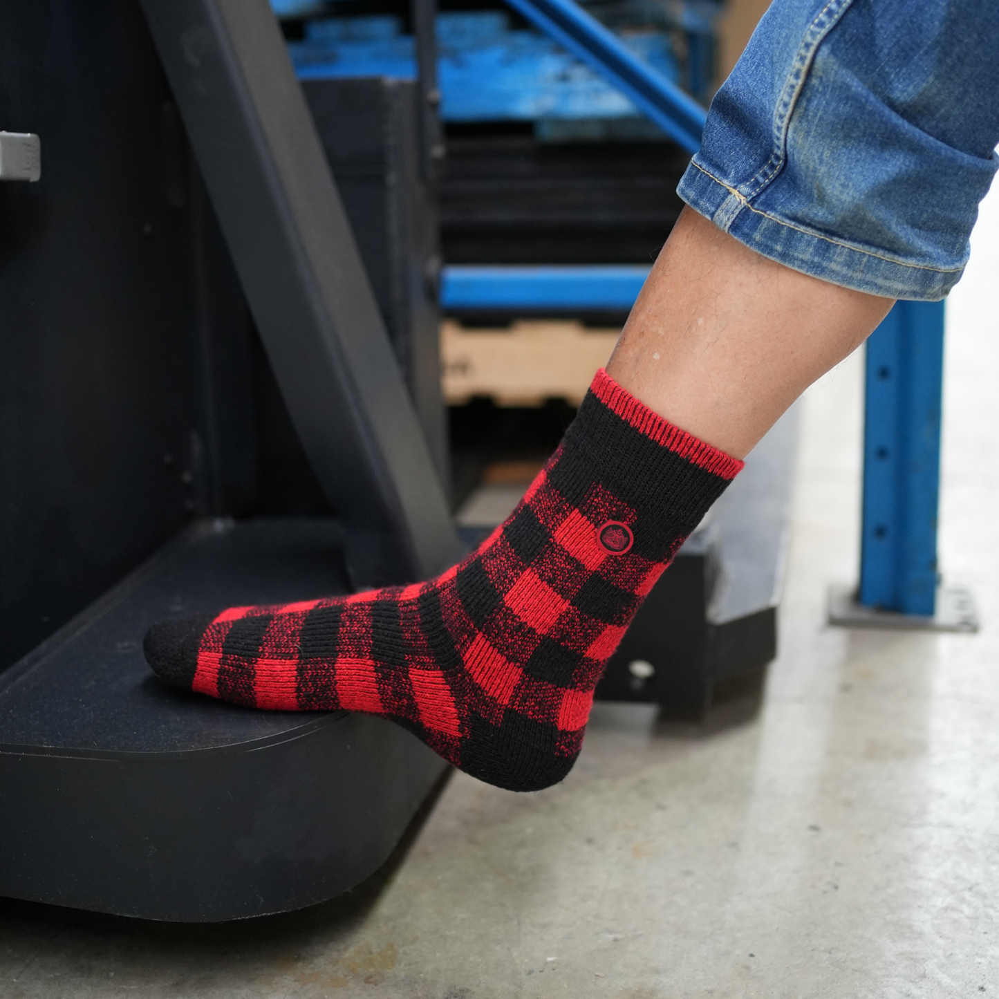 Person wearing Ugly Fish red and black checkered socks with a blue warehouse background.