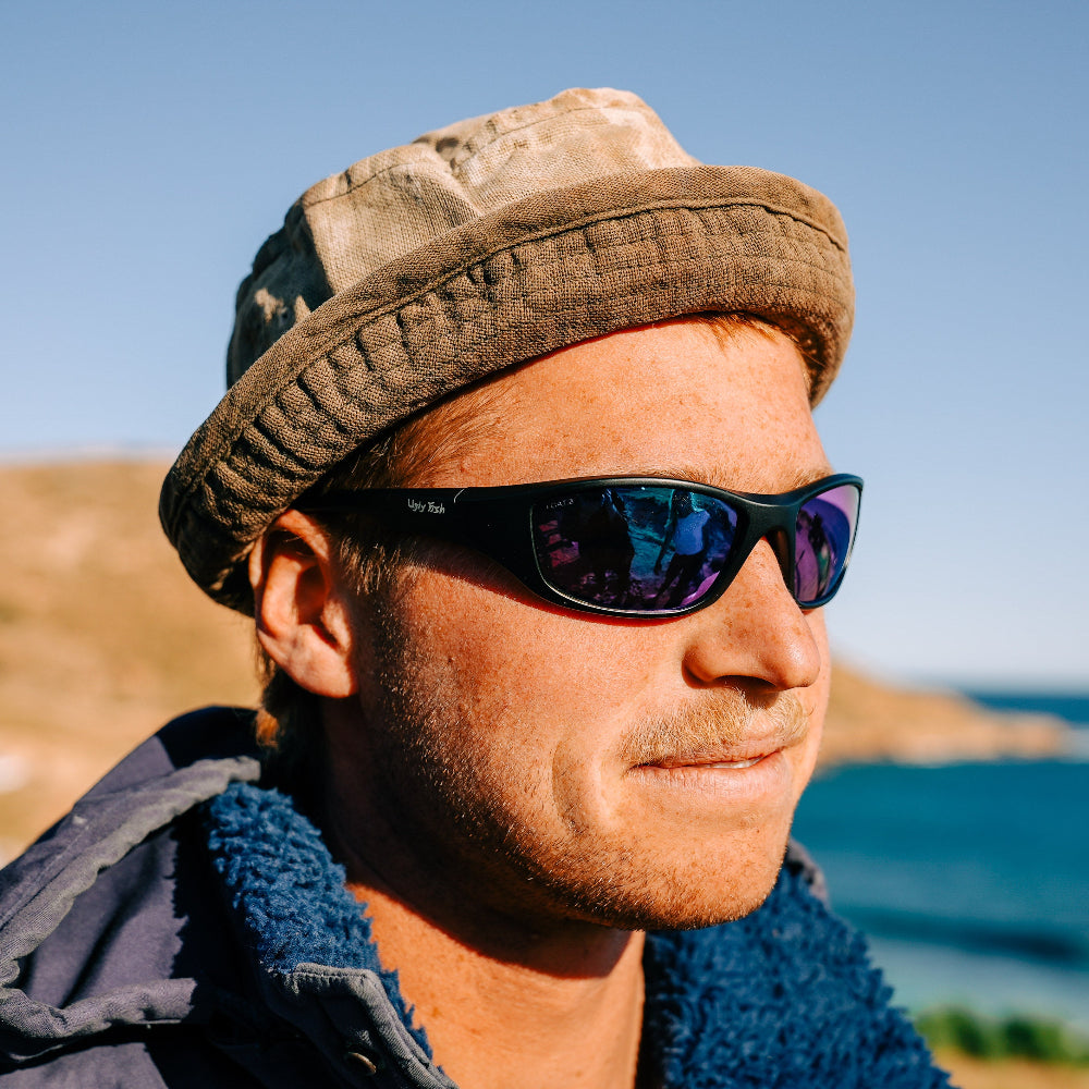 Man wearing Ugly Fish Safety sunglasses with a beach and ocean in the background.