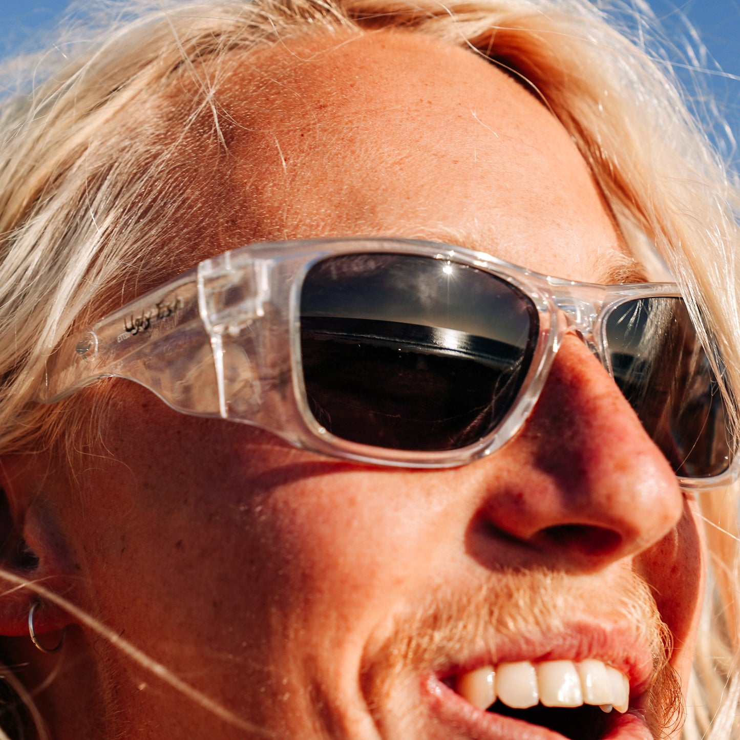Person wearing Ugly Fish Safety sunglasses with a clear lens against a blue sky.