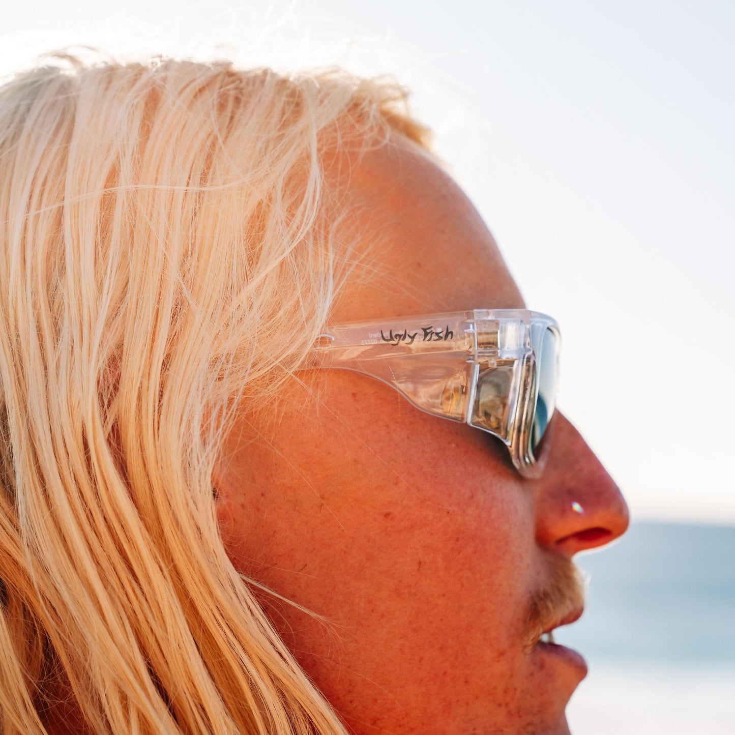 Person wearing clear Ugly Fish Safety sunglasses with a blurred beach background