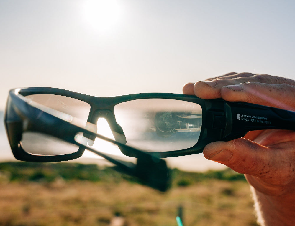 Person holding a pair of Ugly Fish Safety sunglasses with a blurred background.