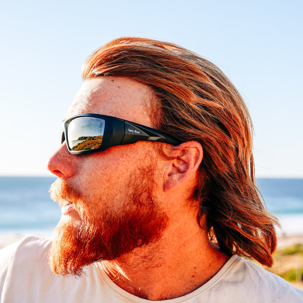 Man wearing Ugly Fish Safety sunglasses with a beach and ocean in the background