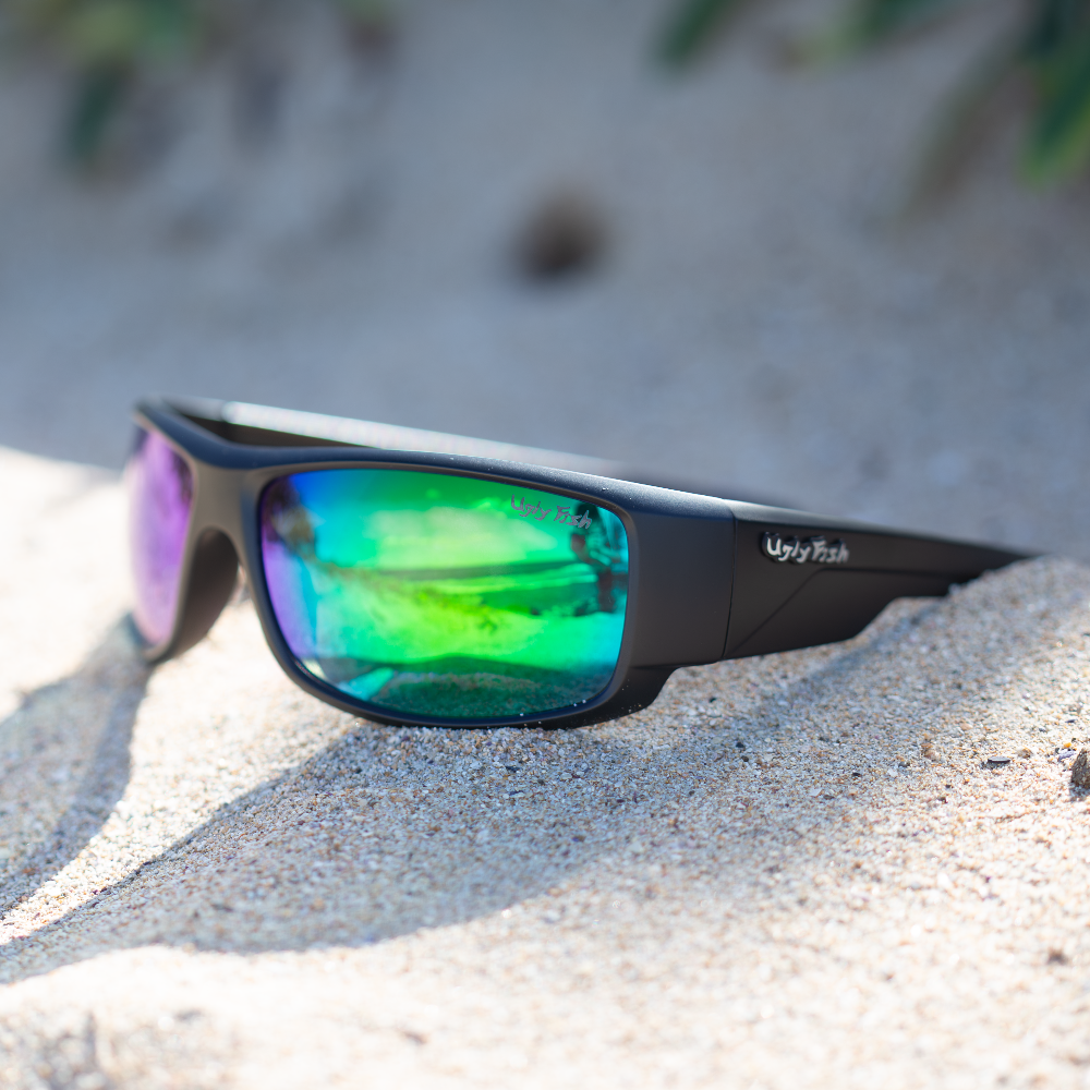 Ugly Fish polarised sunglasses with green reflective lenses on a sandy surface