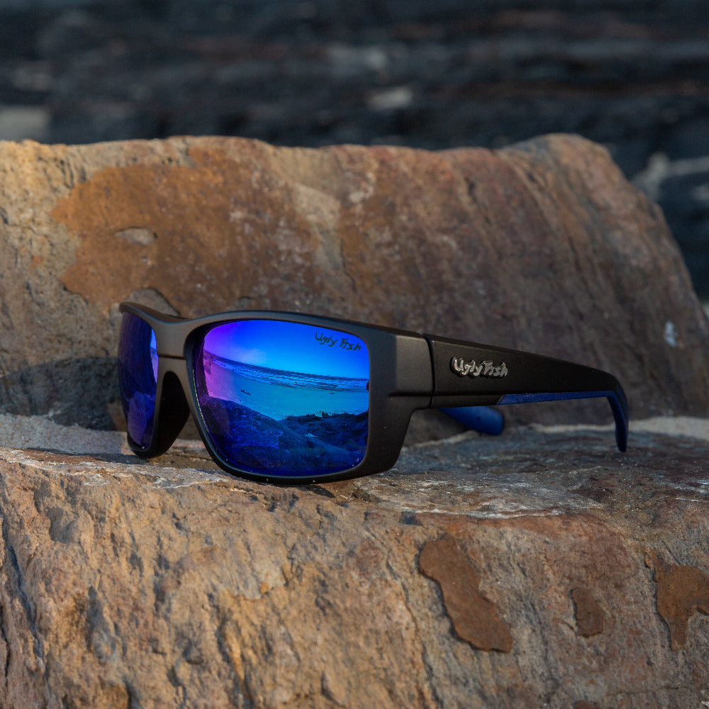 Ugly Fish polarised sunglasses with blue reflective lenses on a rocky surface