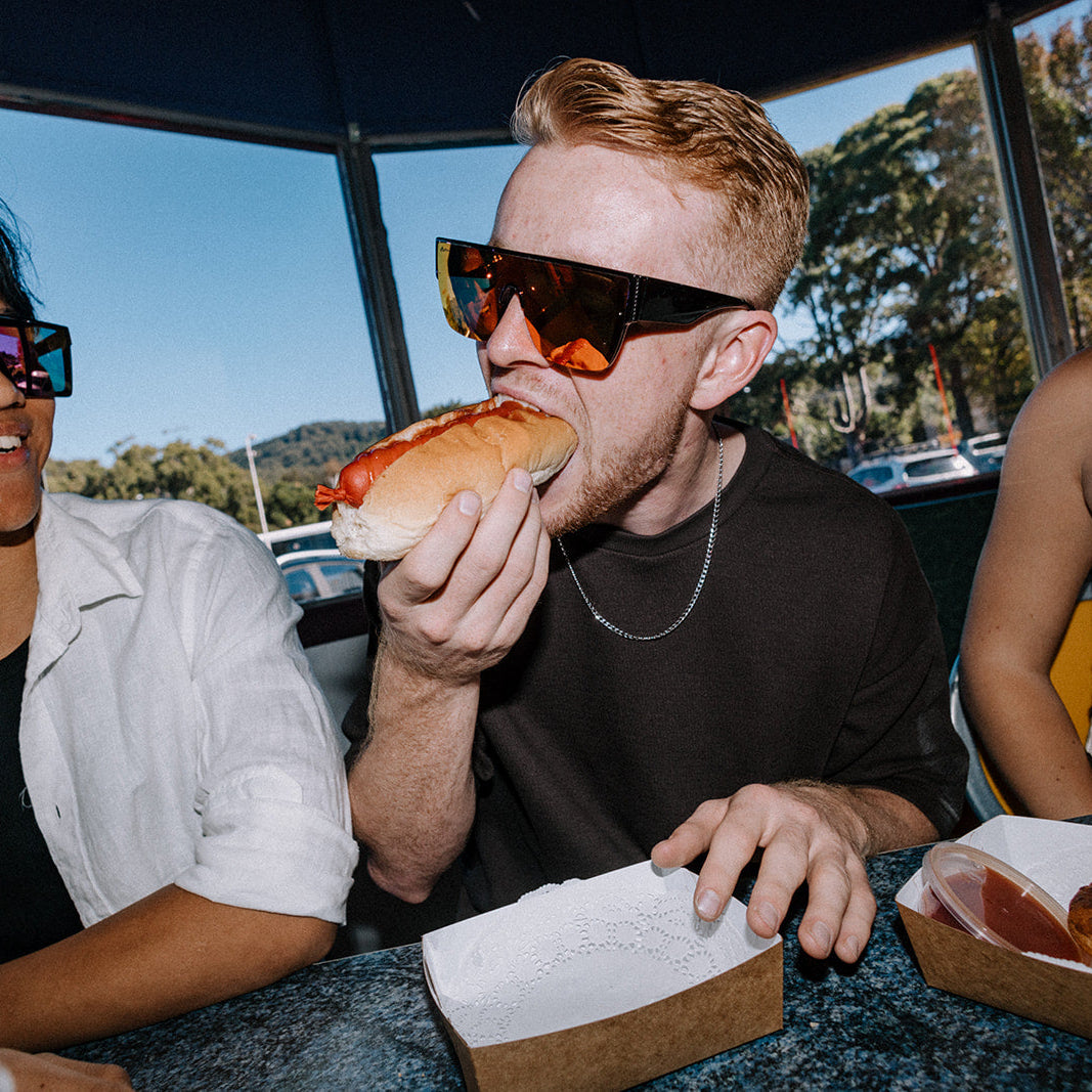 Man enjoying hot dogs wearing Bohemian Retro sunglasses sitting inside a cafeteria.