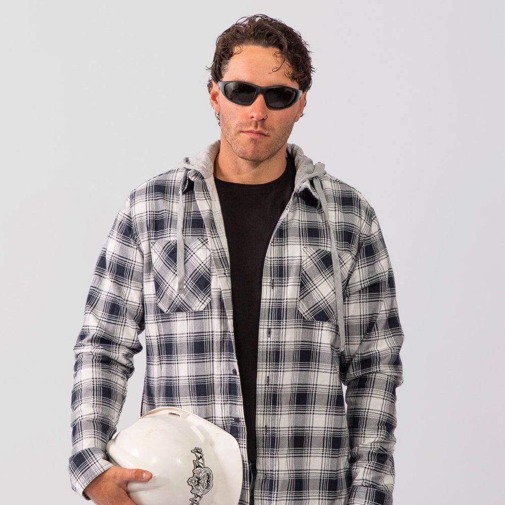 Man wearing a plaid shirt and Ugly Fish safety sunglasses holding a white helmet against a plain background
