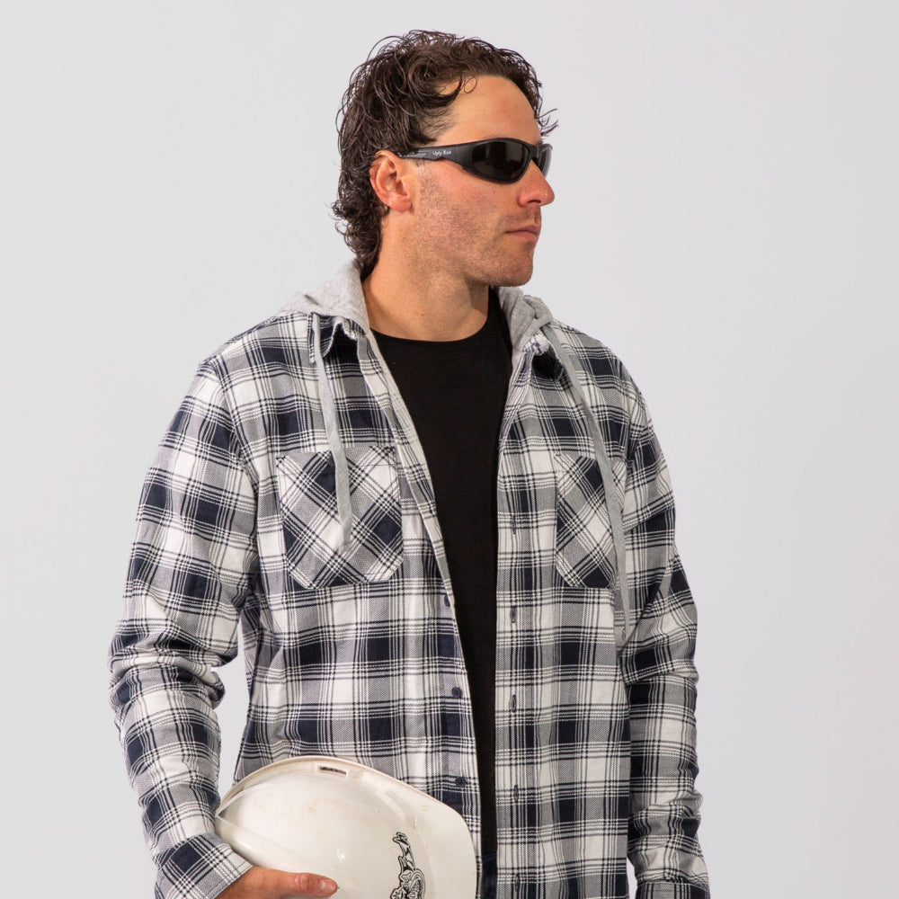 Man wearing a plaid shirt and Ugly Fish Safety sunglasses holding a hard hat against a plain background