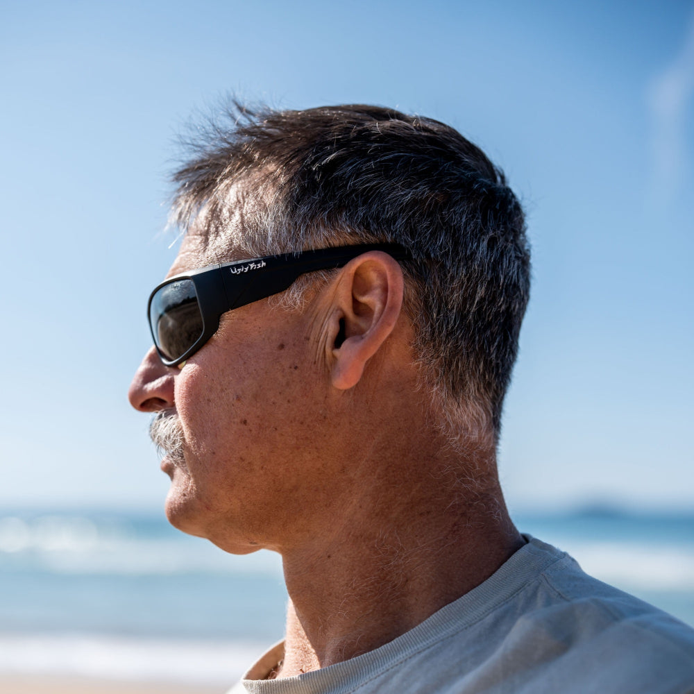 Man wearing Ugly Fish polarised sunglasses with a beach and ocean in the background