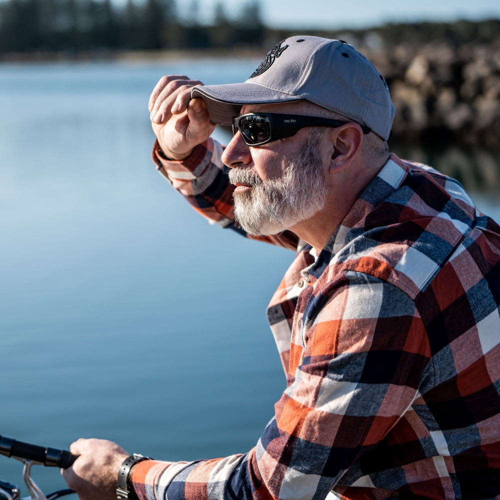 Man wearing Ugly Fish polarised sunglasses and a cap by a body of water