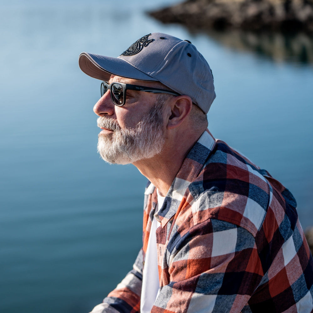 Man wearing Ugly Fish Polarised sunglasses and a cap by a body of water