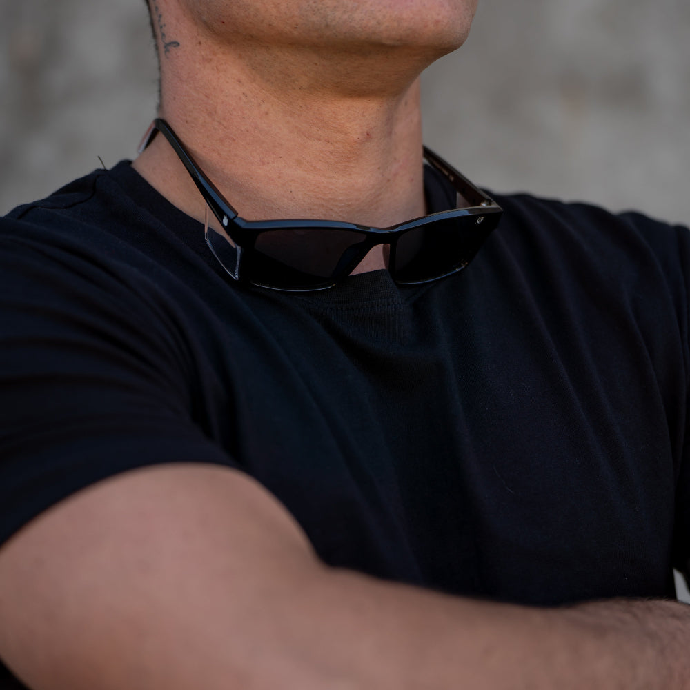 Person wearing a black t-shirt with Ugly Fish Safety sunglasses on their head against a gray background.