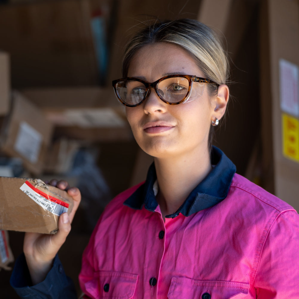 Person in a warehouse setting with cardboard boxes wearing Ugly Fish Safety sunglasses.