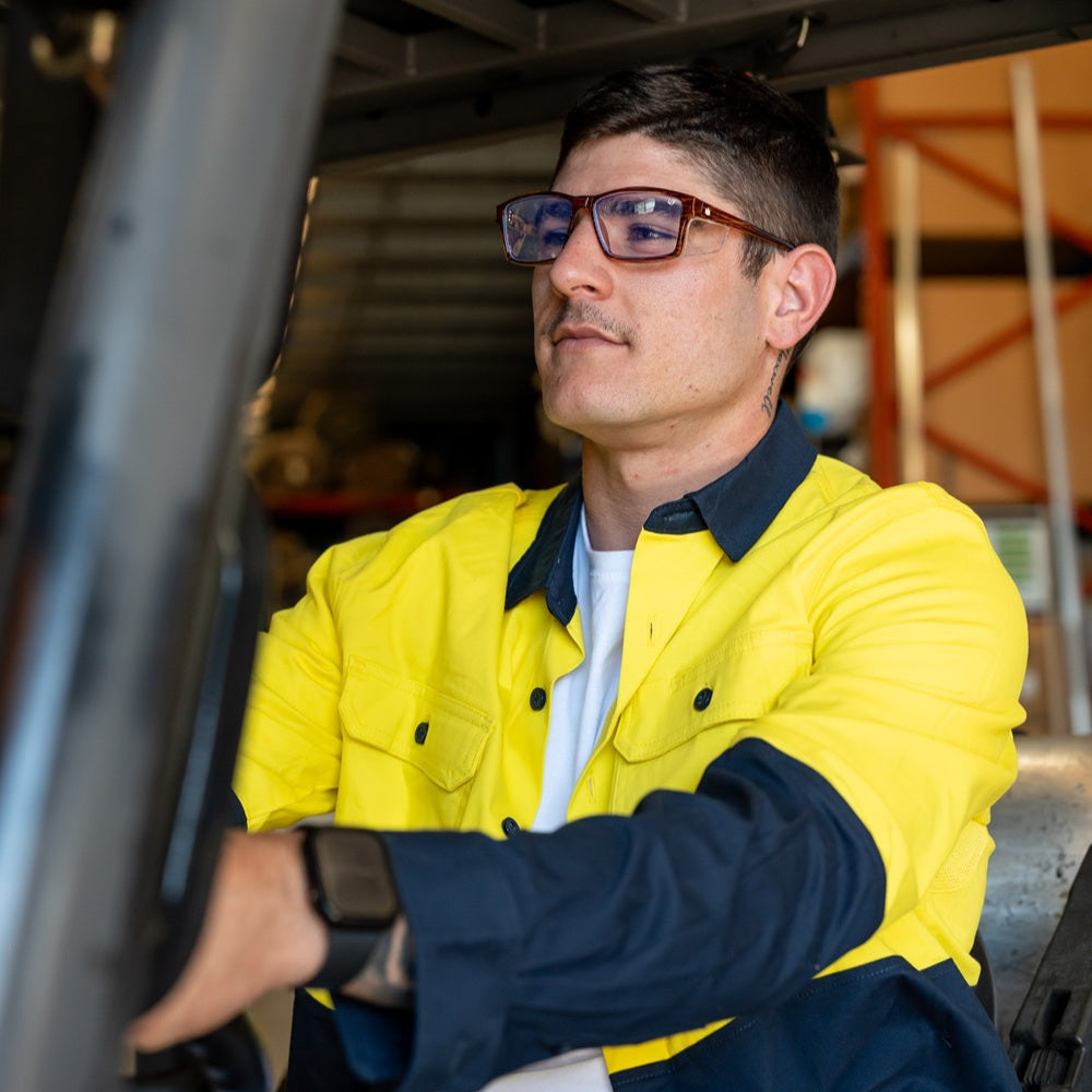 Man wearing a yellow and navy jacket and Ugly Fish safety sunglasses sitting inside a vehicle.