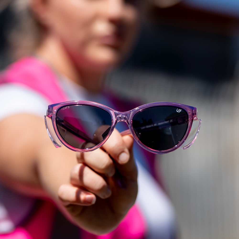 Person holding pink Ugly Fish Safety sunglasses with a blurred background