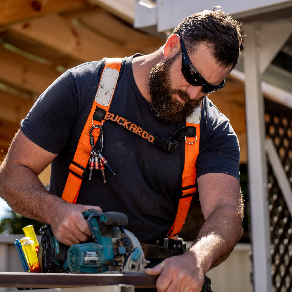 Man wearing Ugly Fish Safety sunglasses using a power tool outdoors.