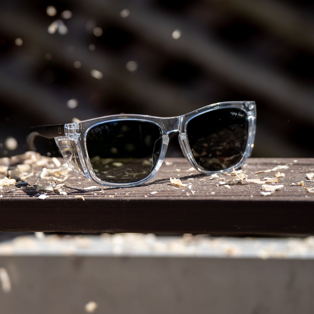 Clear Ugly Fish Safety sunglasses with polarised lenses on a wooden surface with a blurred background