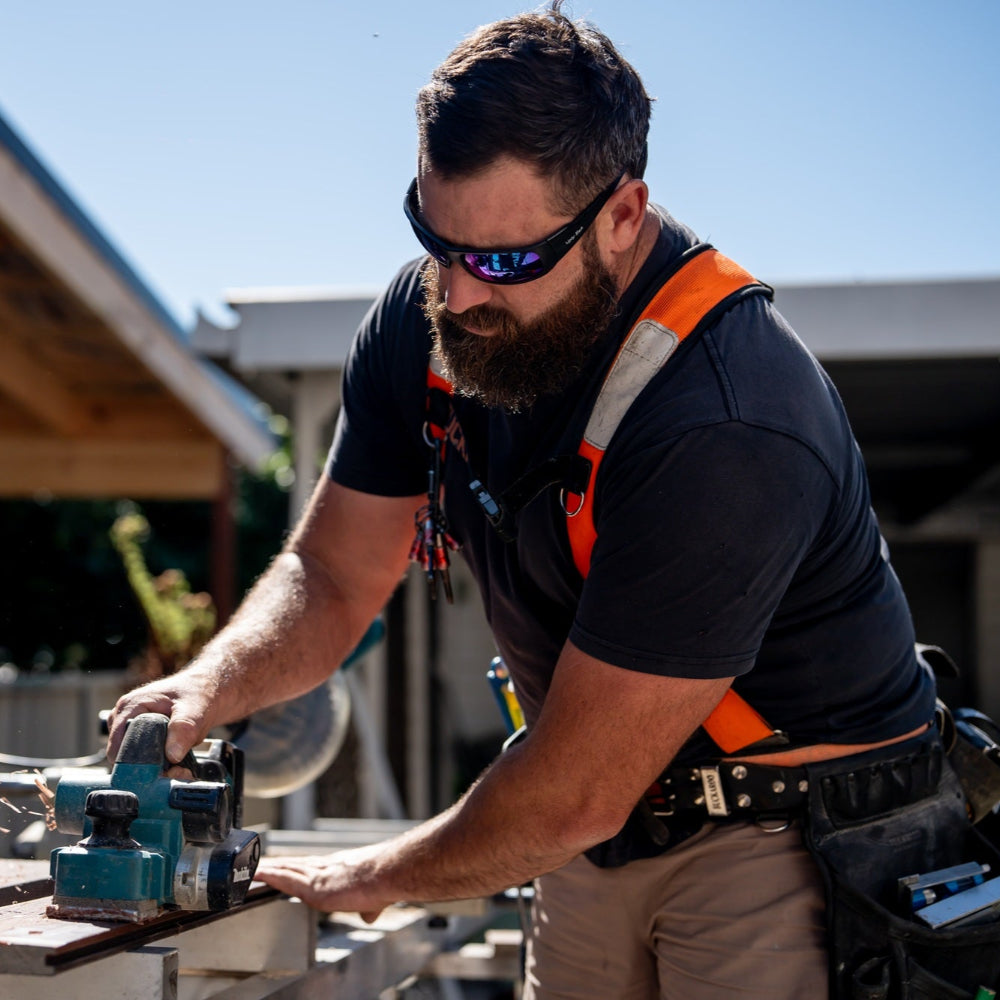 Man using a power tool outdoors wearing Ugly Fish Safety sunglasses with a clear sky background