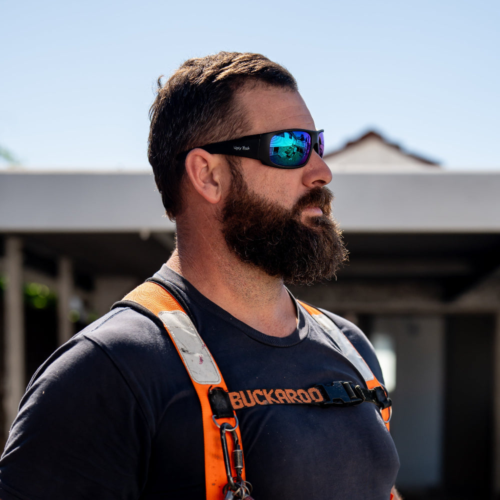 Man wearing Ugly Fish Safety sunglasses and an orange safety vest outdoors.