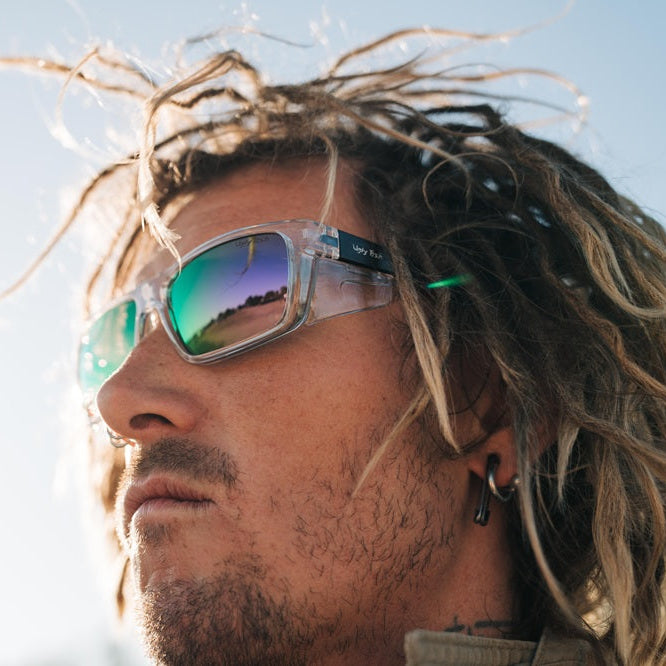 Person with dreadlocks wearing Ugly Fish Safety sunglasses against a blurred natural background