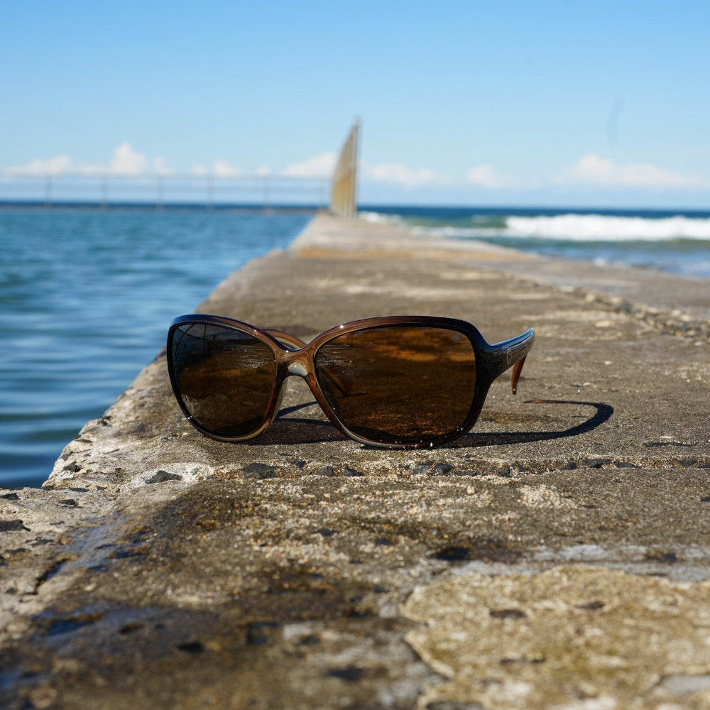 Ugly Fish polarised sunglasses on a concrete ledge with ocean and sky in the background.