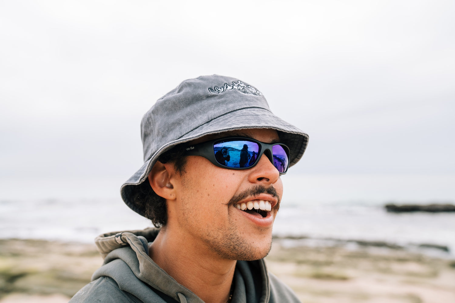 Person wearing a gray bucket hat and sunglasses outdoors with a blurred natural background
