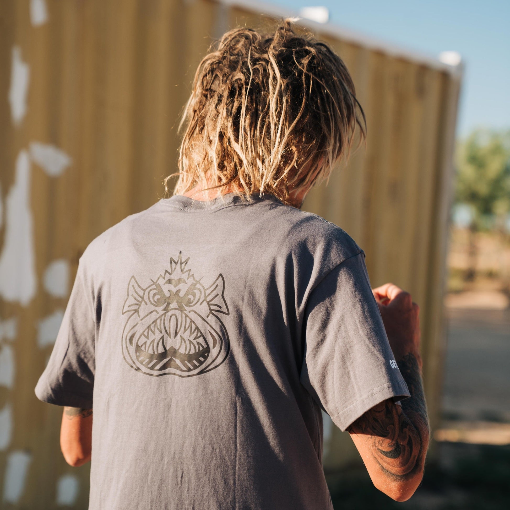 Person wearing a grey t-shirt with an Ugly Fish logo on the back, standing in front of a beige wall.