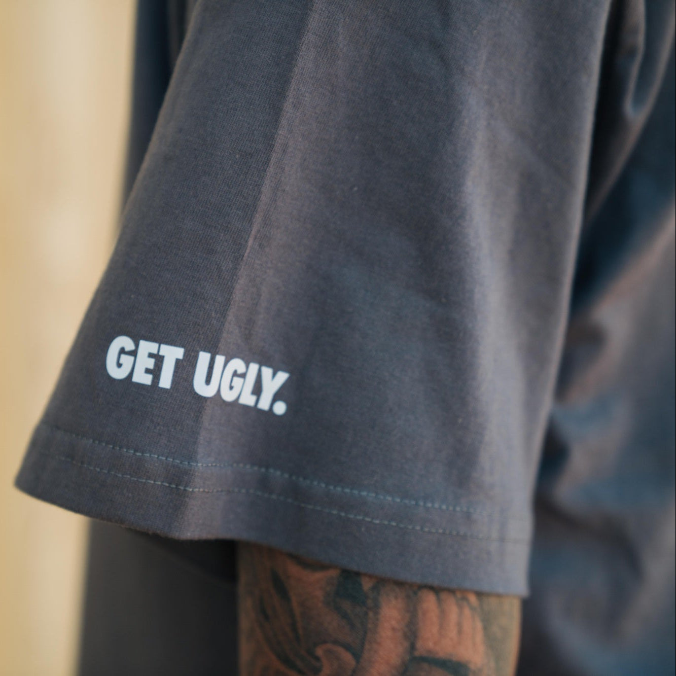 Grey shirt with 'GET UGLY.' text on a blurred background
