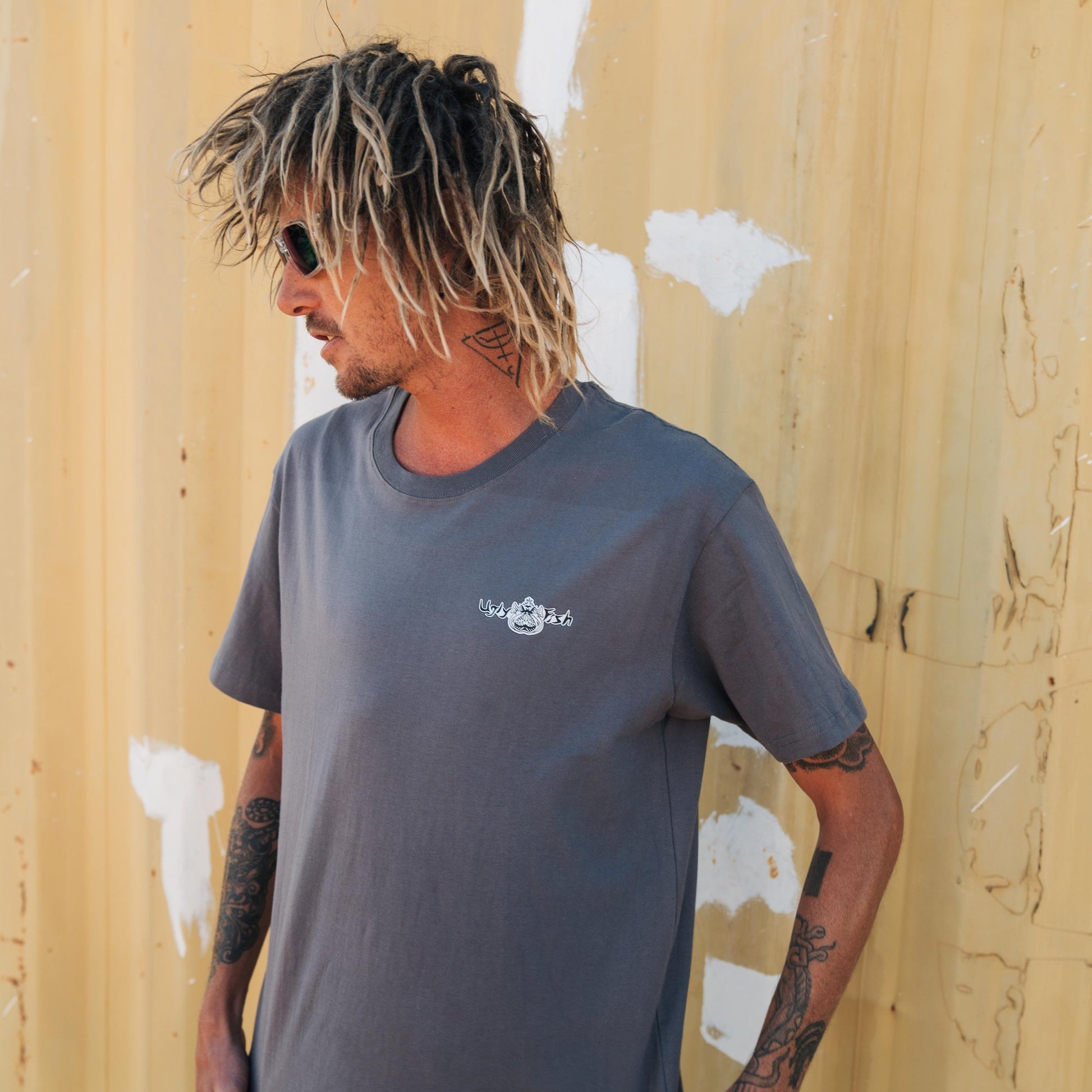 Man wearing a grey t-shirt with an Ugly Fish logo against a yellow wall.