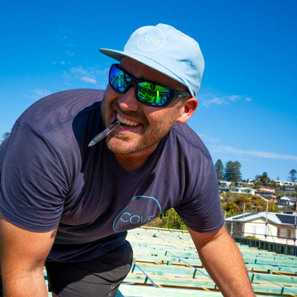 Man wearing Ugly Fish Safety sunglasses, leaning on a railing with a clear blue sky in the background