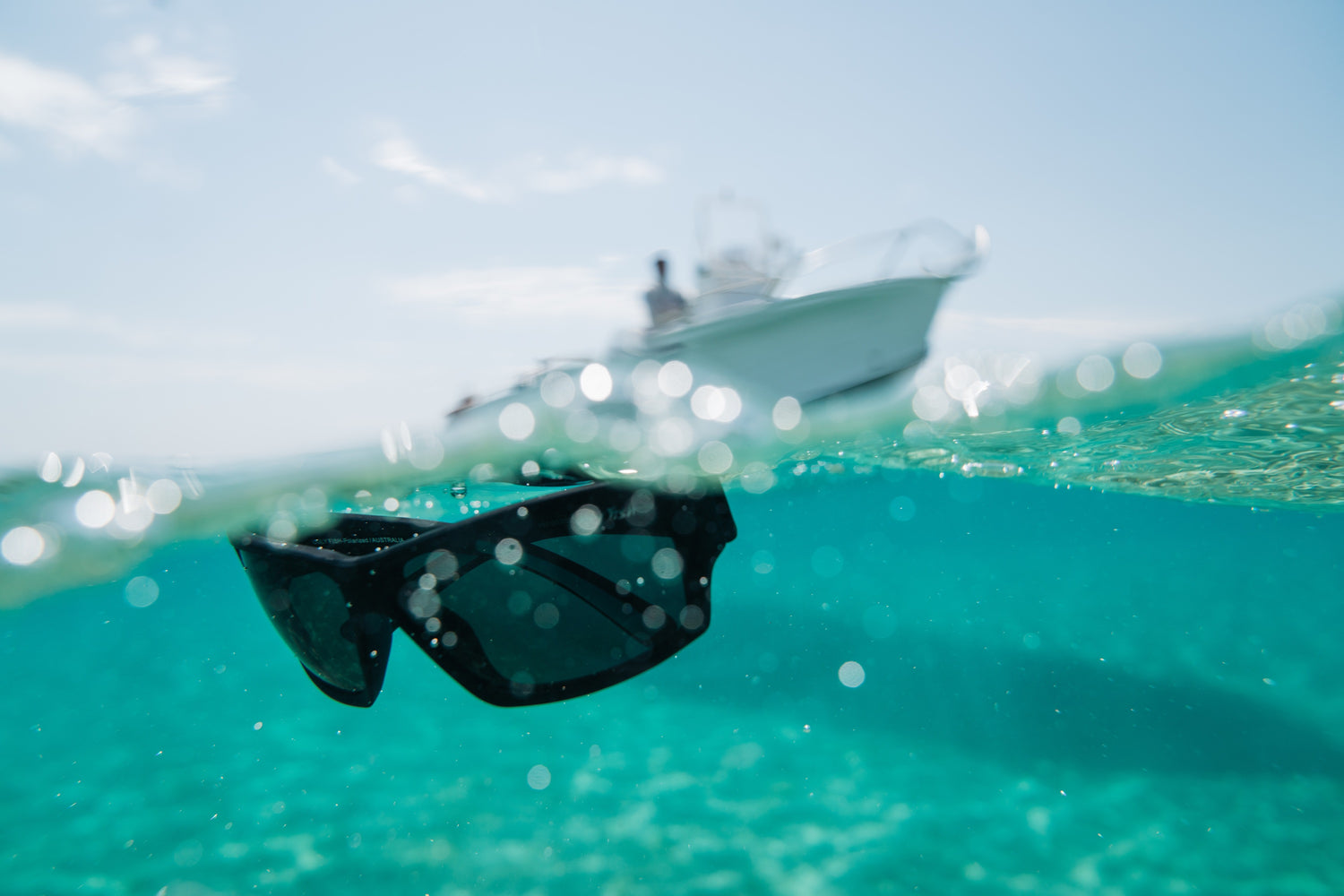 Black sunglasses floating in clear blue water with a boat in the background