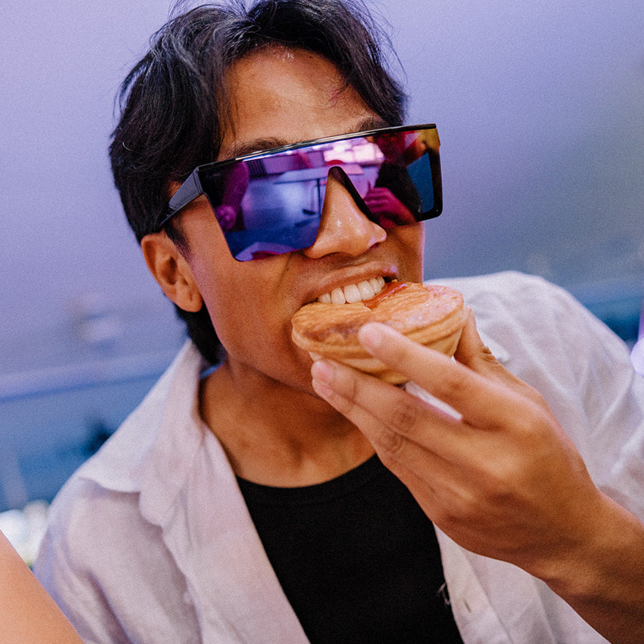Person eating a pie with colorful Rogue sunglasses on, surrounded by friends.