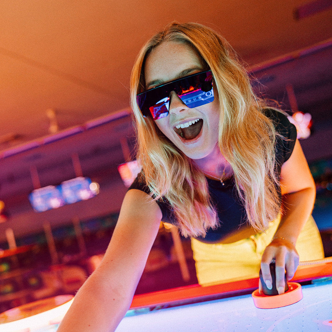 Person playing air hockey with a smile, wearing Rogue sunglasses.