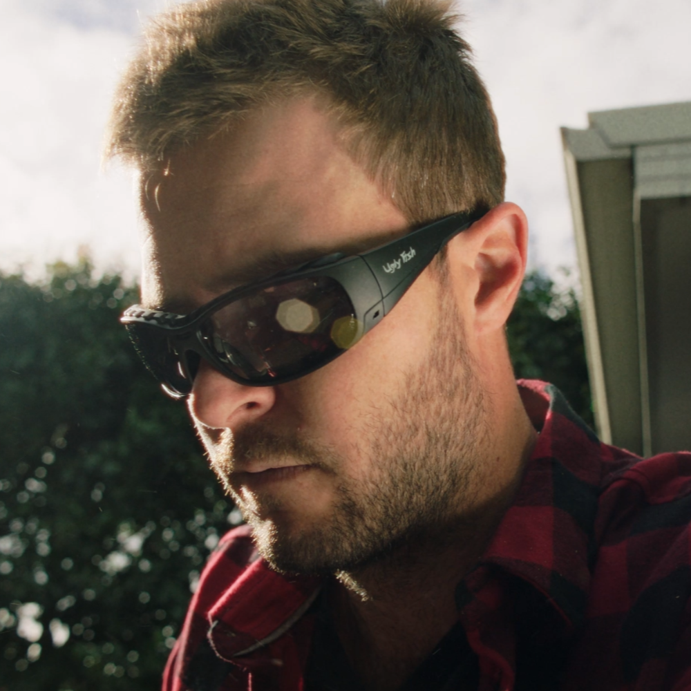 Man wearing Ugly Fish Safety sunglasses and a red shirt outdoors.