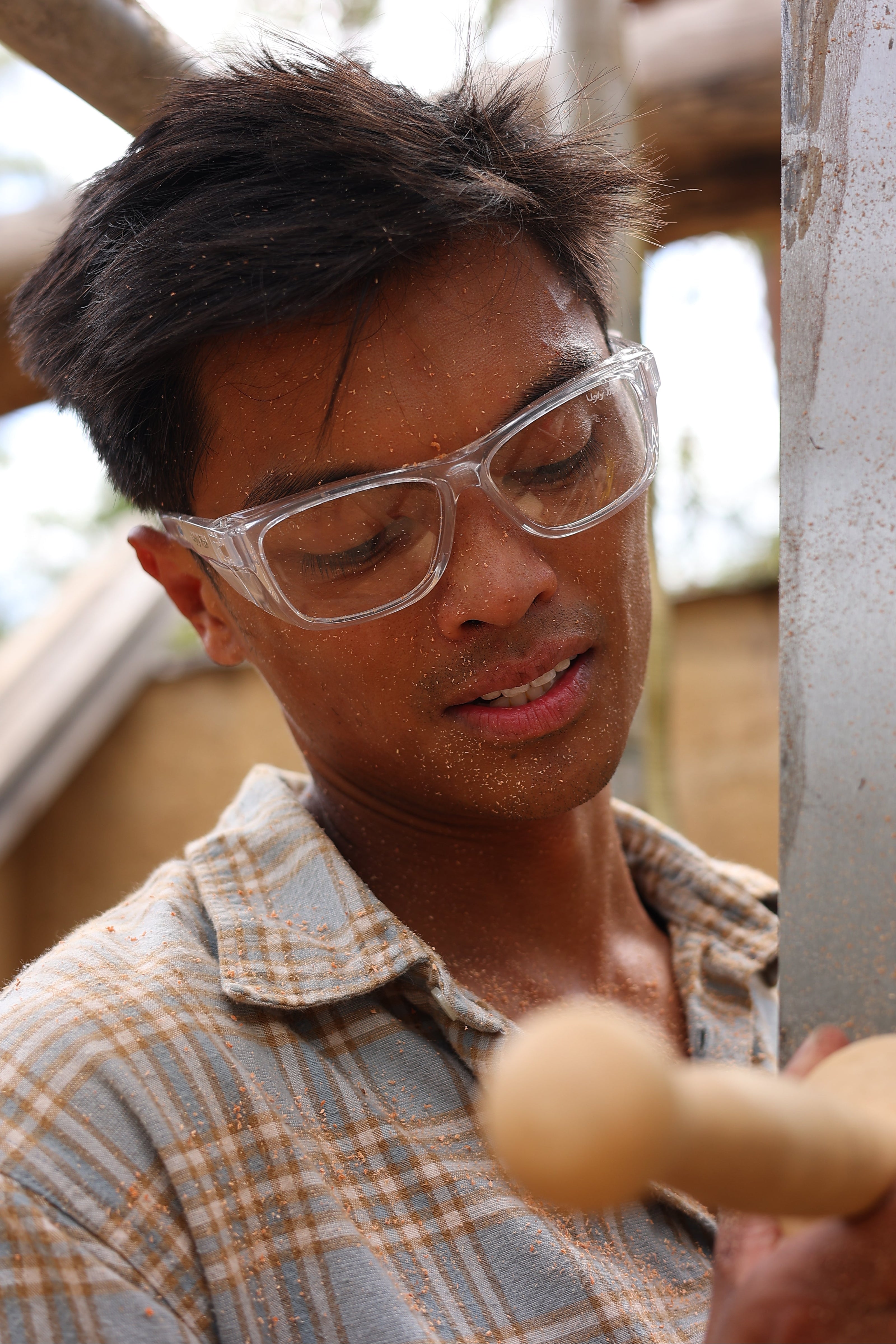 Person wearing safety goggles and holding a wooden object, likely in a workshop setting.