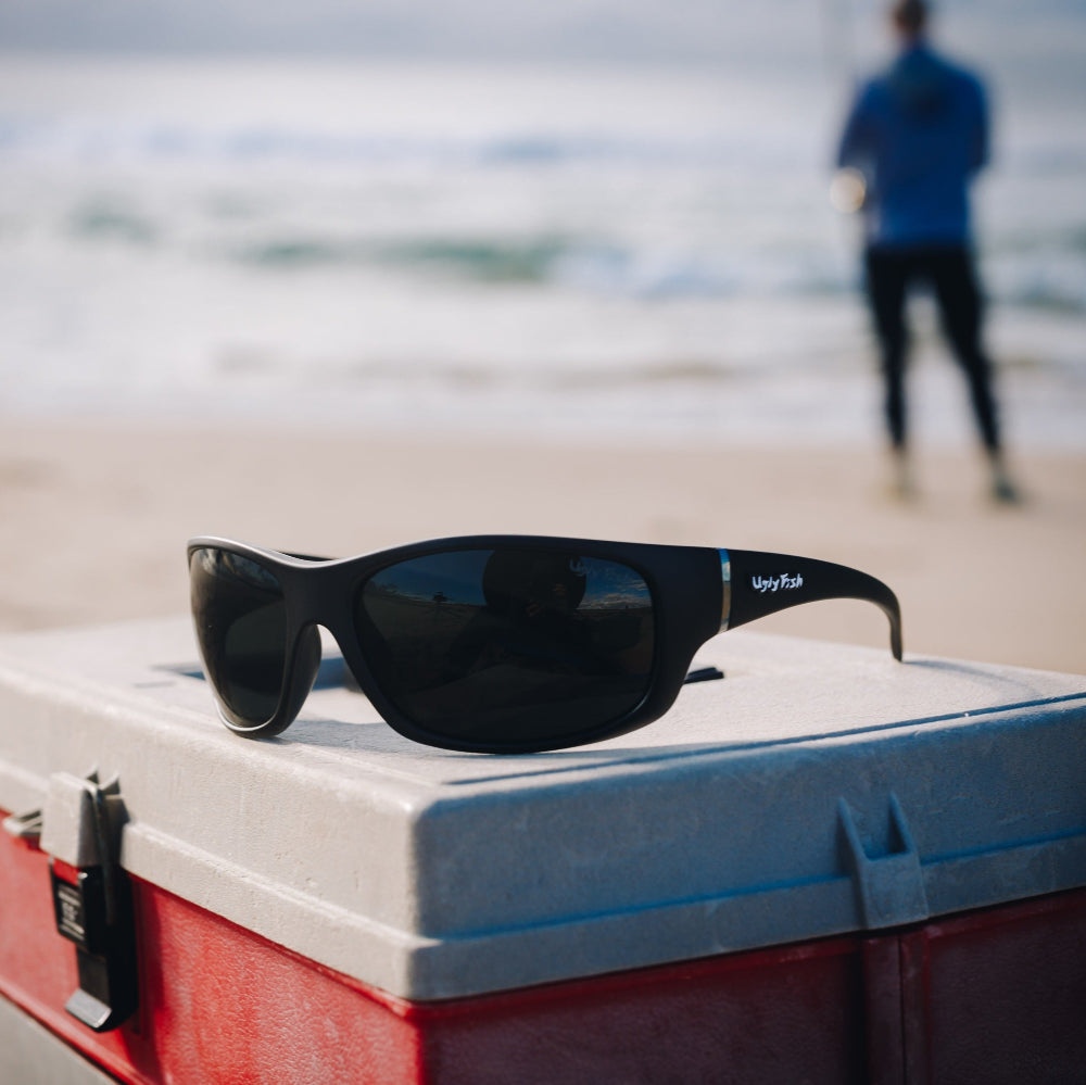 Ugly Fish Polarised sunglasses on a cooler with a beach and person in the background.