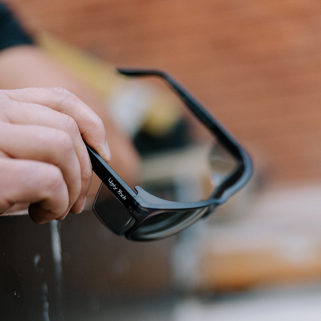 Person holding black Freestone safety sunglasses with Ugly Fish branding against a blurred background