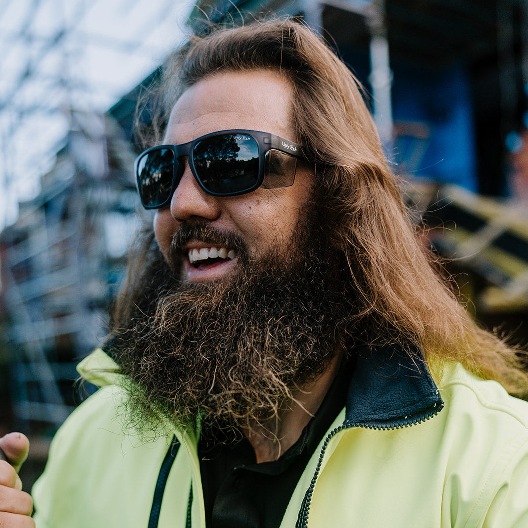 Man with long hair and beard wearing Ugly Fish Freestone safety sunglasses and a high-visibility jacket.