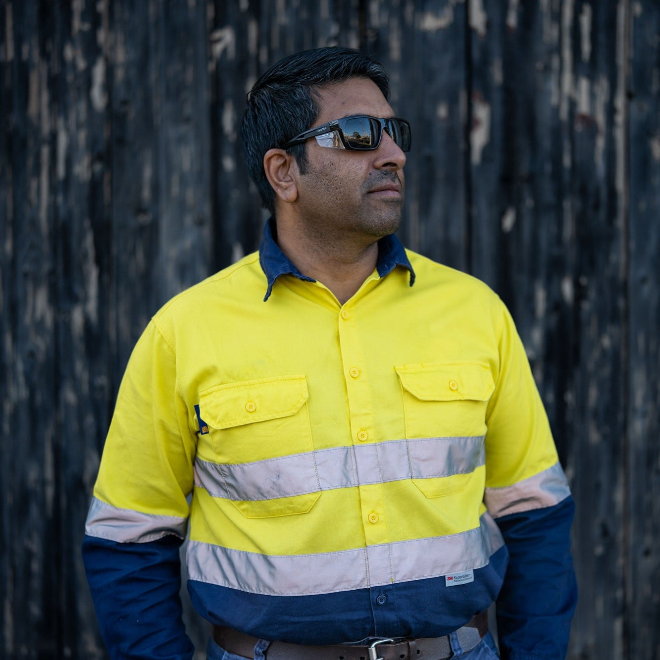 Person wearing a high-visibility yellow work shirt against a dark textured background