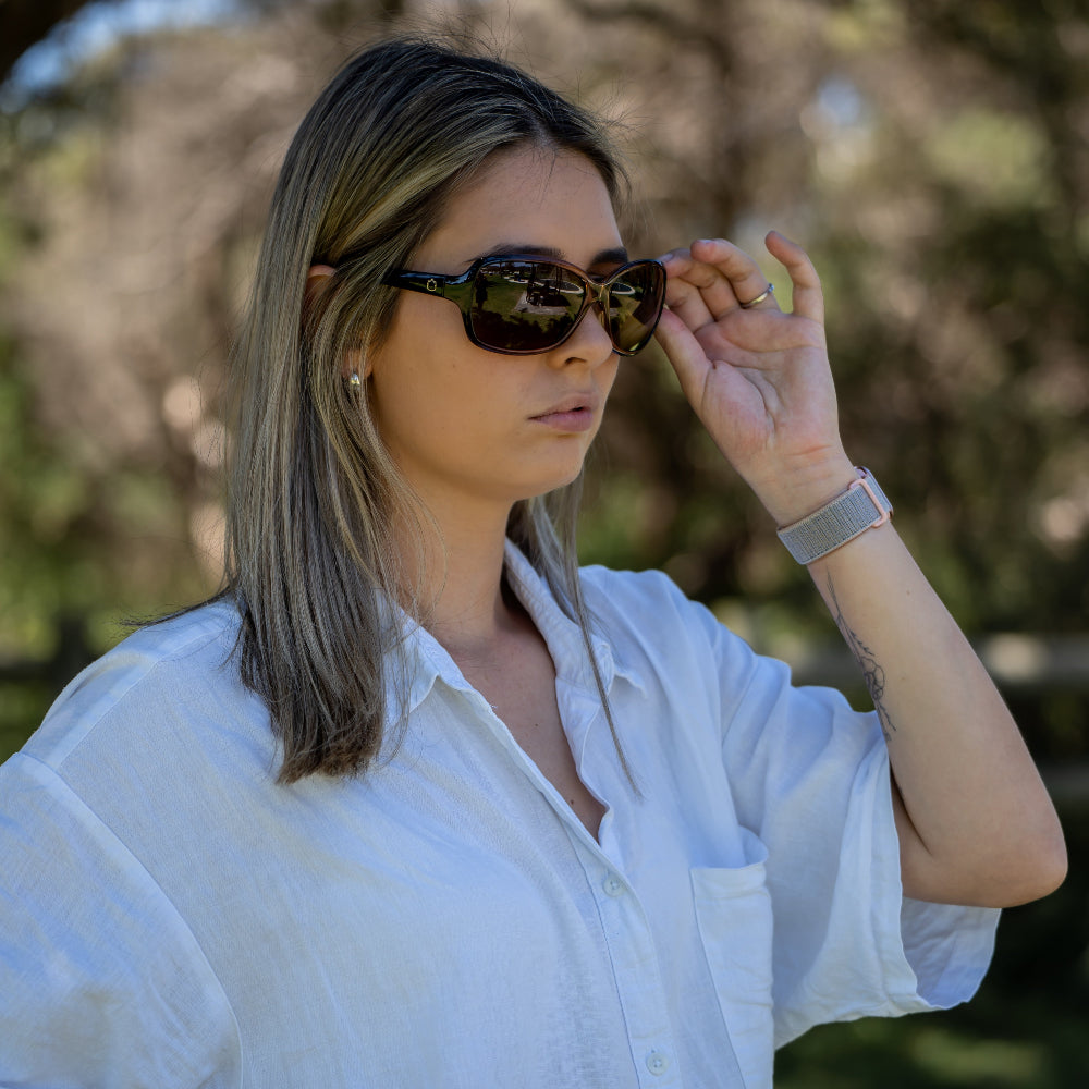Woman adjusting Ugly Fish polarised sunglasses outdoors with trees in the background