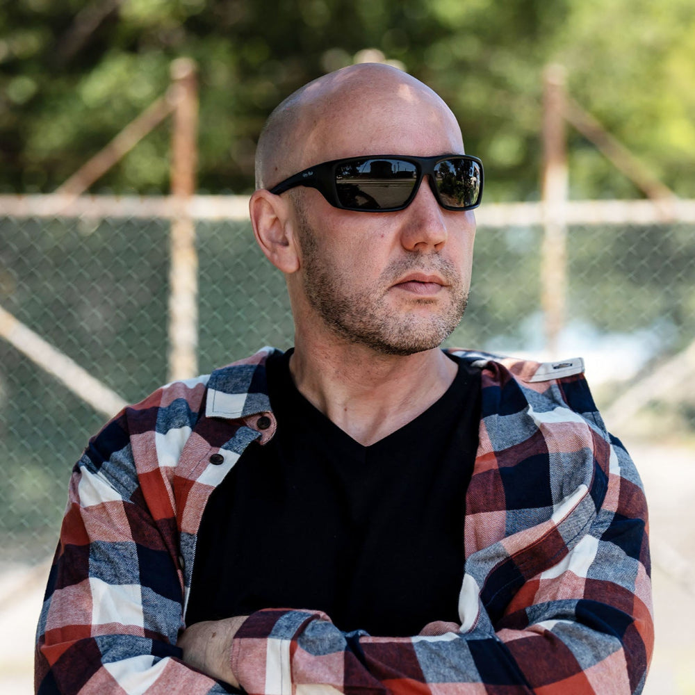 Man wearing Ugly Fish Safety sunglasses and a plaid shirt with a blurred background.