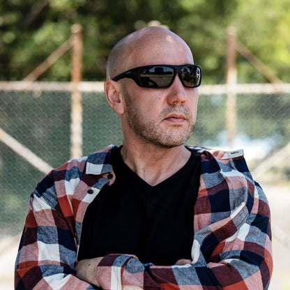 Man wearing Ugly Fish Safety sunglasses and a plaid shirt with a blurred background.