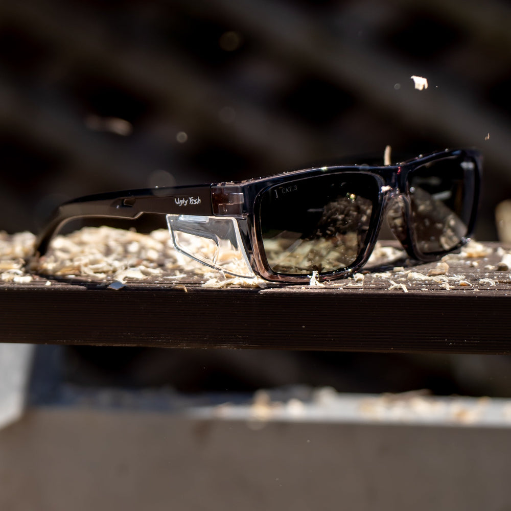 Black Ugly Fish safety sunglasses with polarised lenses on a wooden surface with a blurred background