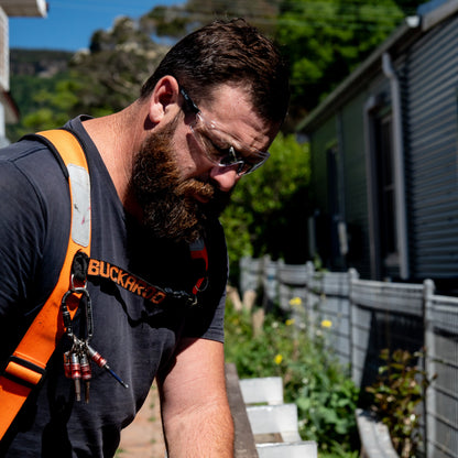 Man using a power tool wearing Ugly Fish safety shields on a wooden surface outdoors.